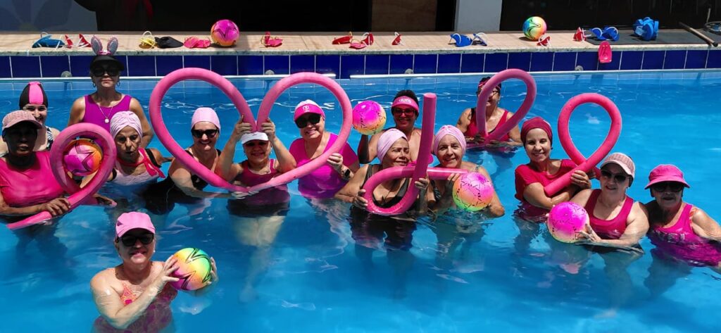 Alunas da Academia Andréa Maestri formam coração com espaguetes rosa na piscina no Outubro Rosa