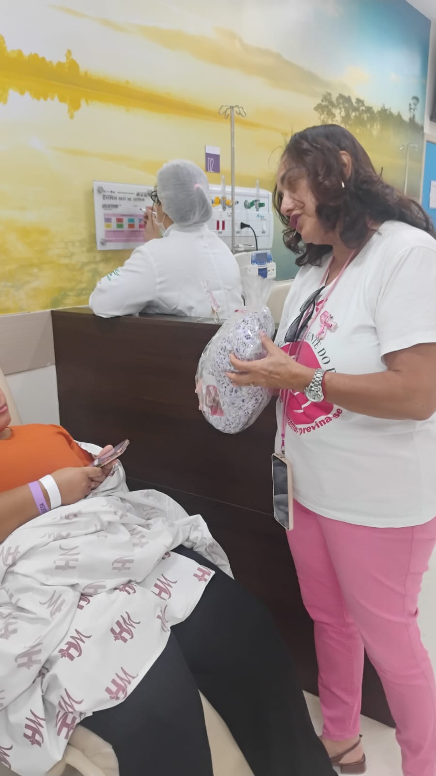 Voluntária da ASBEM entrega almofada de coração a paciente na sala de quimioterapia do Hospital da Mulher