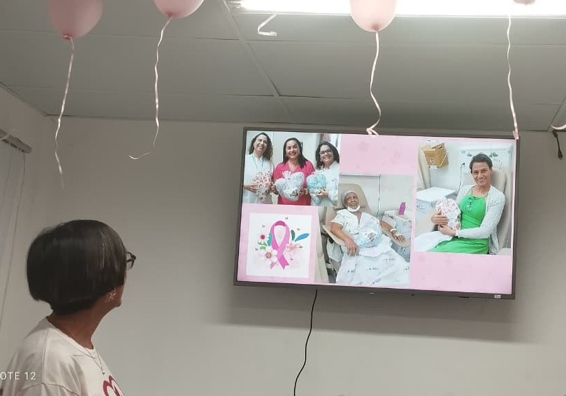 Telão da palestra na Embasa mostra fotos das entregas de almofadas de coração da ASBEM