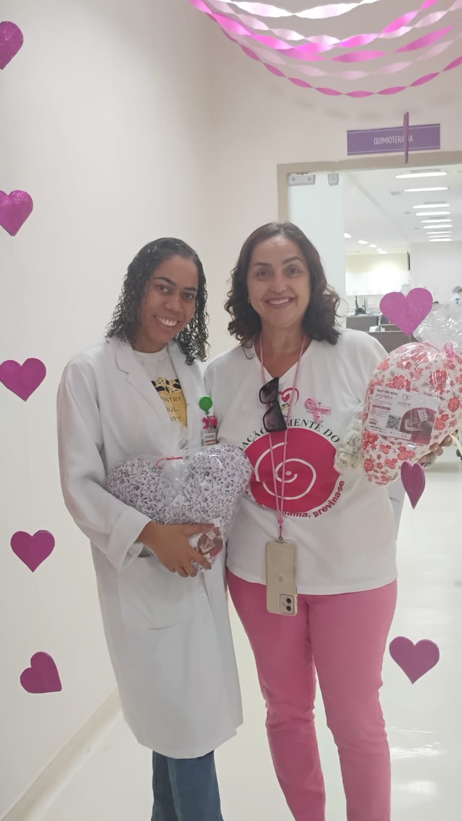 Profissional do Hospital da Mulher e voluntária da ASBEM com almofadas de coração no corredor decorado para o Outubro Rosa