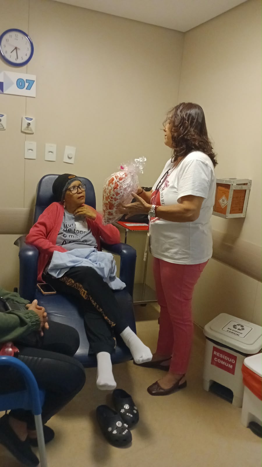 Voluntária da ASBEM apresenta a almofada de coração a uma paciente na quimioterapia do Irmã Dulce