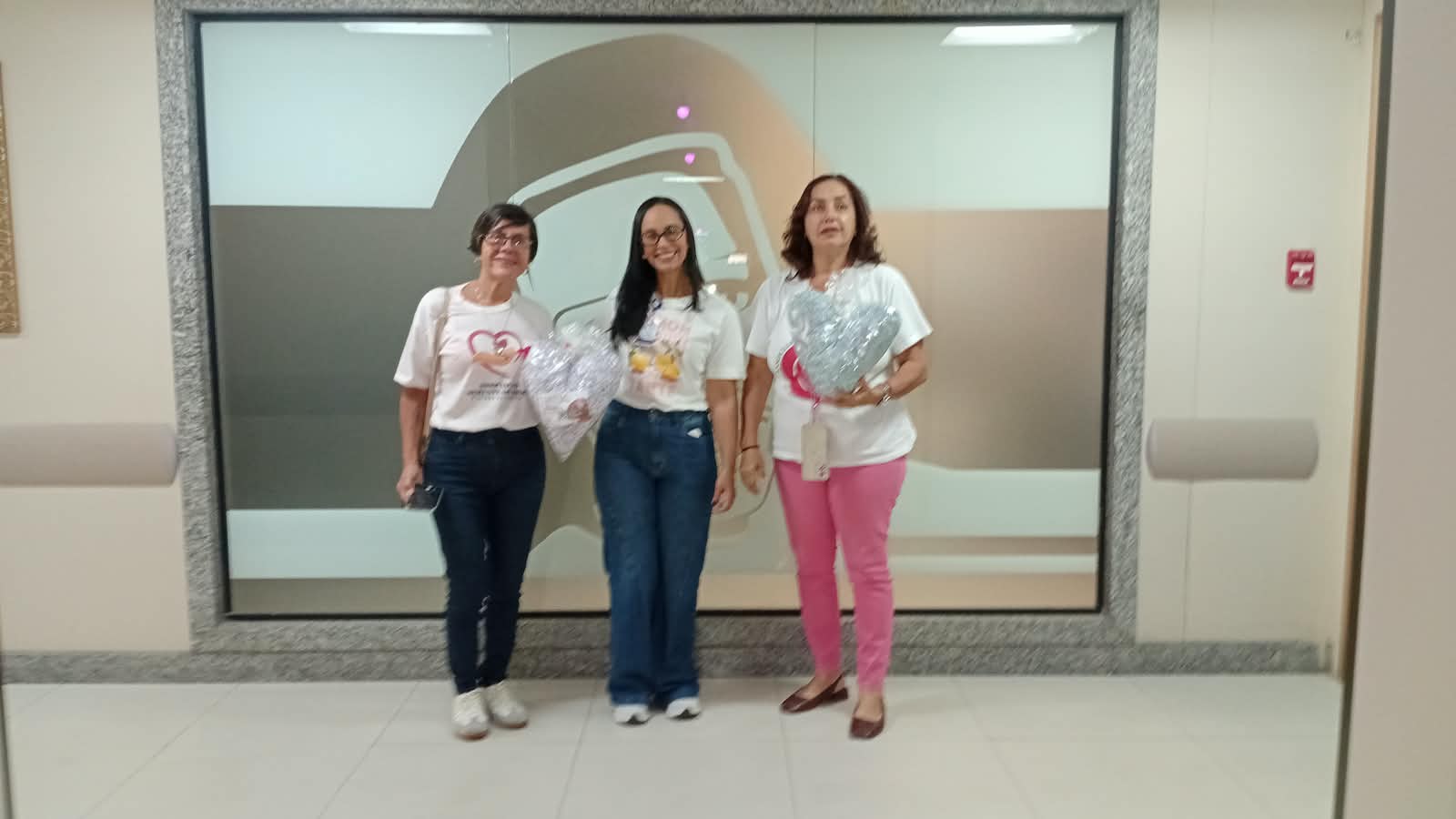 Voluntárias da ASBEM em frente à imagem de Irmã Dulce segurando almofadas de coração
