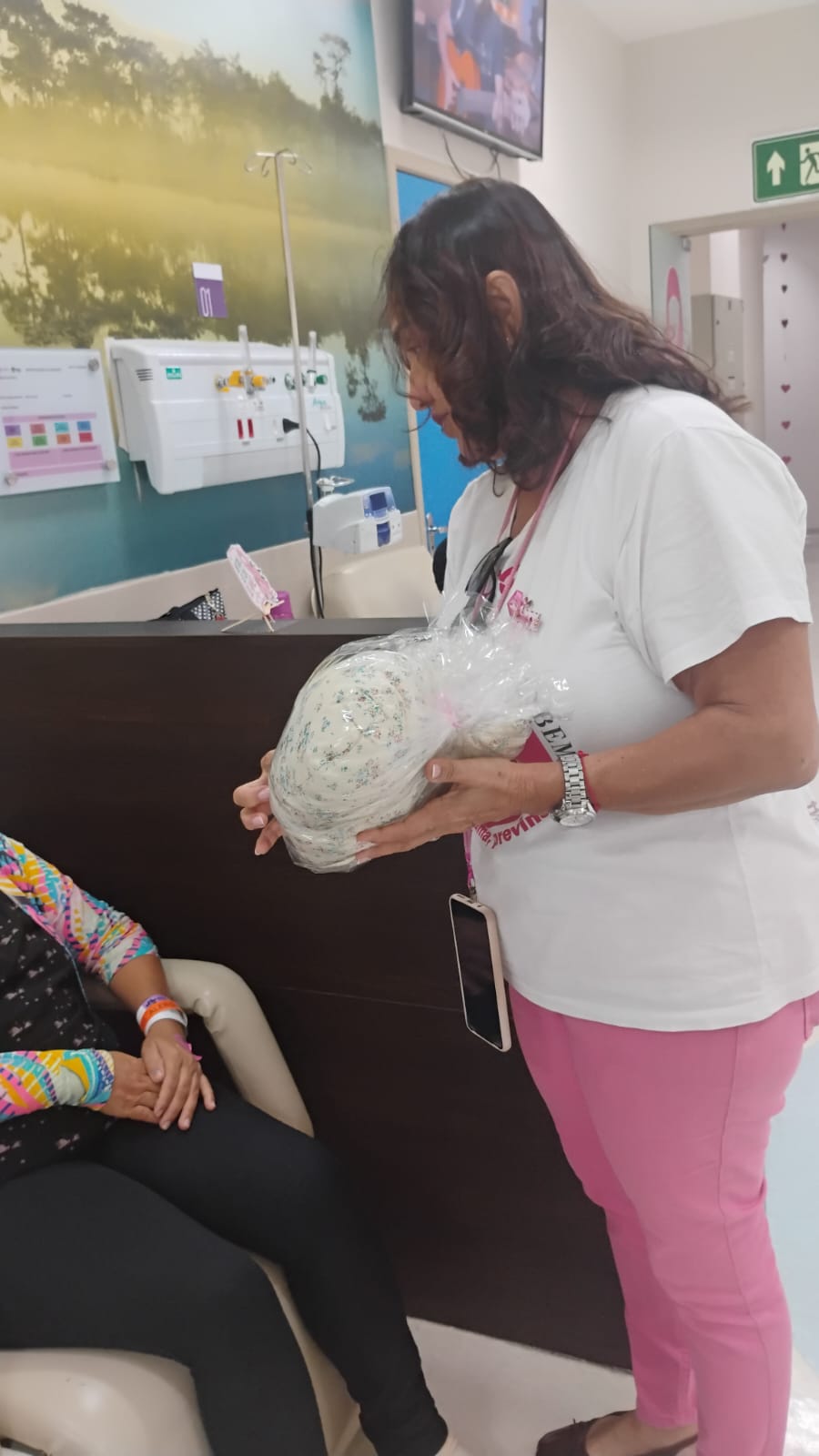 Voluntária da ASBEM apresenta a almofada de coração a uma paciente em tratamento