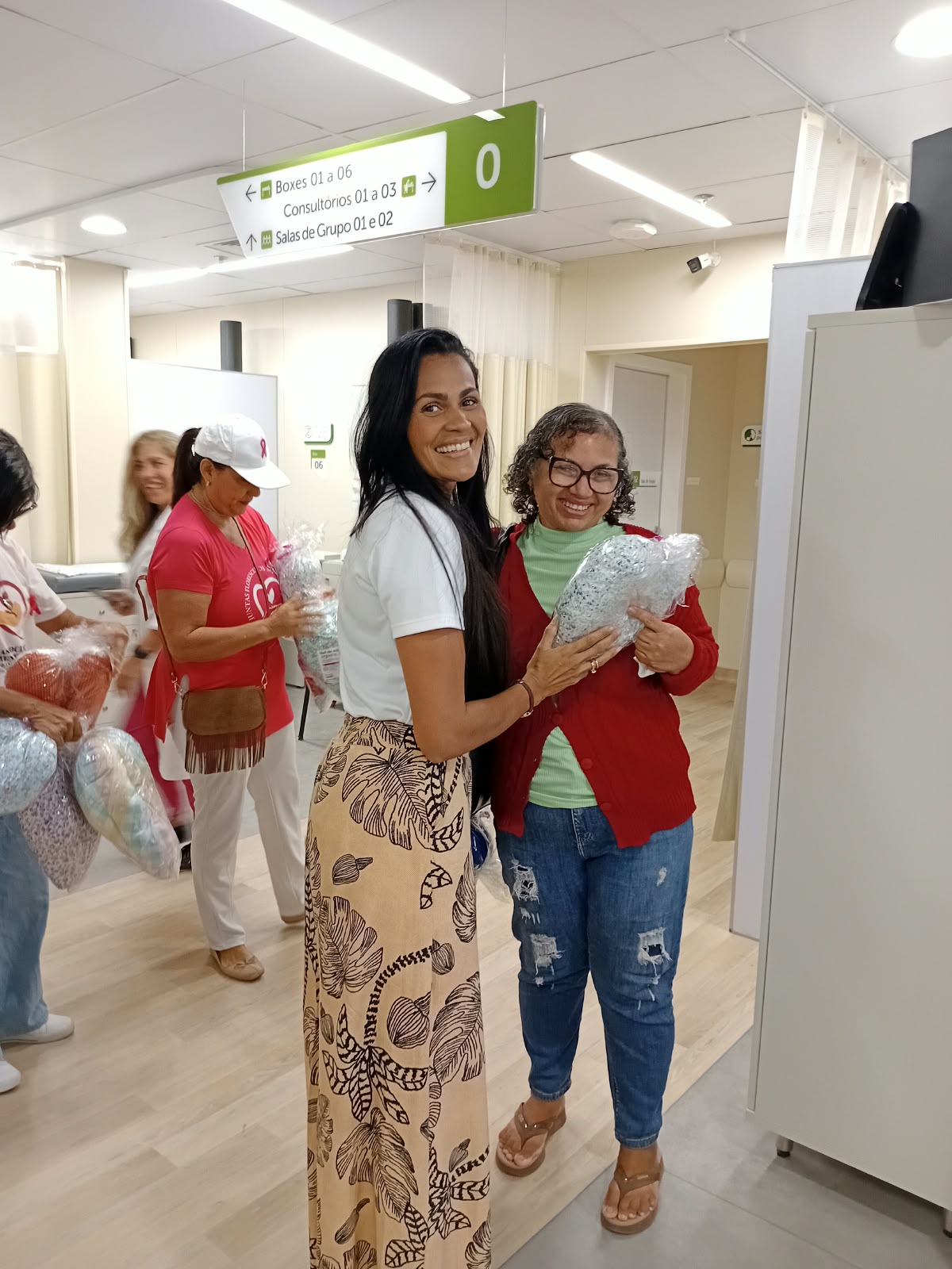 Voluntária da ASBEM entrega almofada de coração a paciente na recepção do Hospital Aristides Maltez
