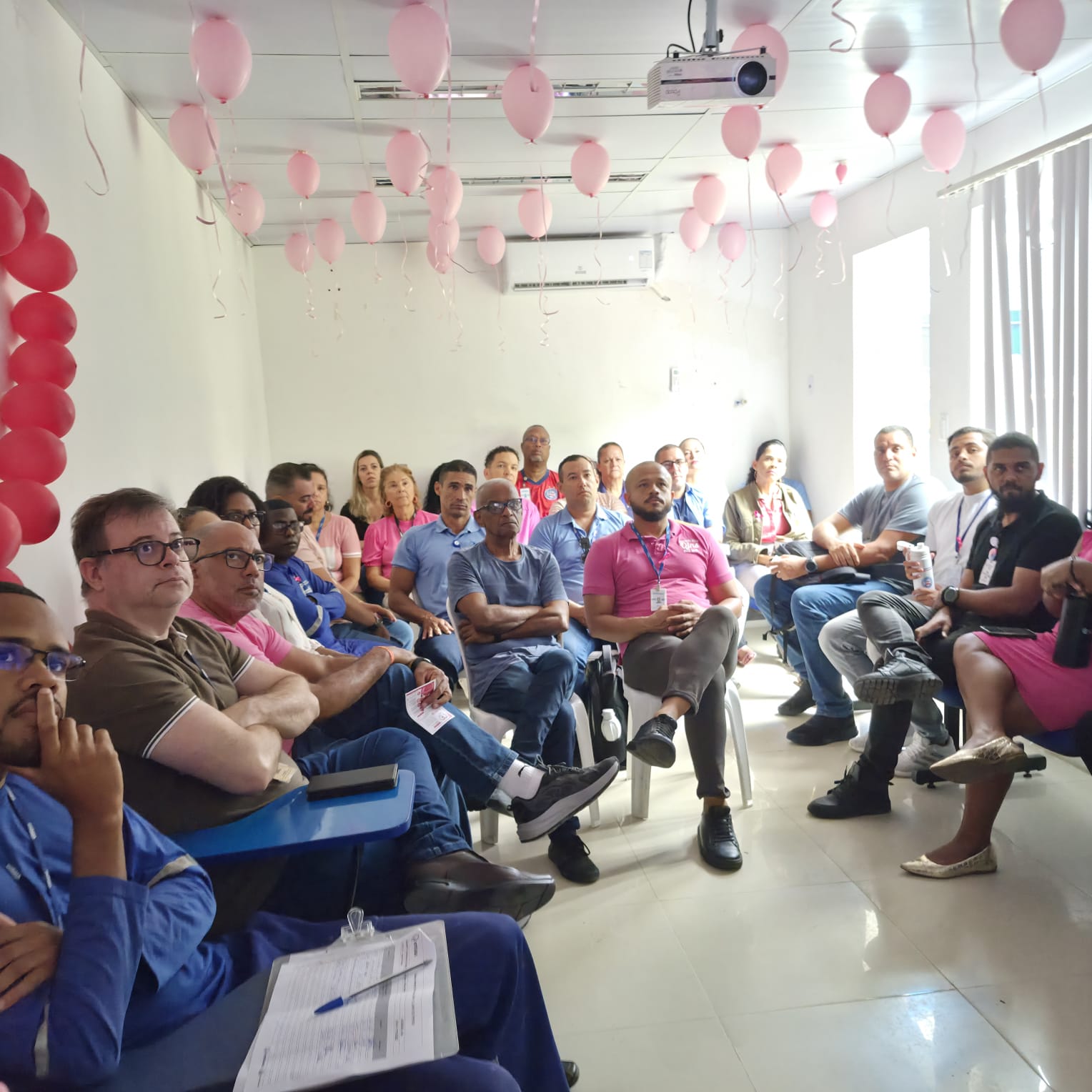 Colaboradores da Embasa acompanham a palestra sobre câncer de mama em sala decorada com balões rosa